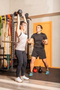 personal trainer: Woman doing shoulder exercise with dumbbells in the gym. Concept of exercise with equipment at gym.