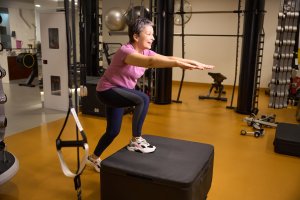 Cross-Training Effect: Middle aged smiling caucasian woman wearing sportswear doing sport exercise on sport box in gym. Concept of modern healthy lifestyle